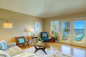 A living room with a sofa, a coffee table, a chair, a lamp, a plant, and a view of the ocean through large sliding doors.