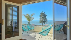 Ein Balkon mit Meerblick, ausgestattet mit einer Schiebeglastür, zwei türkisblauen Stühlen und einer kleinen Palme.