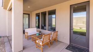 Um pátio externo com mesa, cadeiras, um banco e uma porta com vista para o exterior.