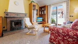 Een woonkamer met een open haard, een televisie, een bank en een balkon met uitzicht op gebouwen.