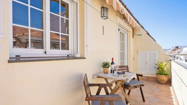 Een balkon met een tafel, stoelen, een bloempot en een fles wijn.