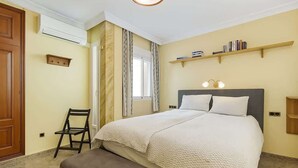 Een slaapkamer met een bed, een stoel, een plank met boeken en een raam met gordijnen.