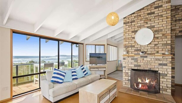 A modern living room with a fireplace, a sofa with striped pillows, a television, and a large window overlooking a scenic view.