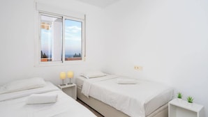 Ein schlicht eingerichtetes Schlafzimmer mit zwei Betten, einem Fenster mit Aussicht, Nachttischlampen und einer kleinen Pflanze auf einem Nachttisch.