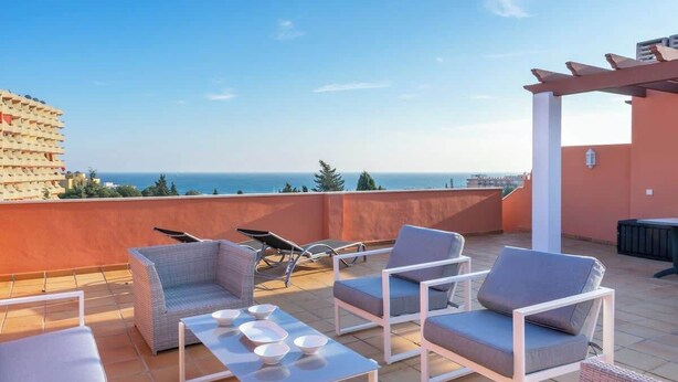 Eine Dachterrasse mit Sitzgelegenheiten im Freien, einer Pergola und Blick auf das Meer.