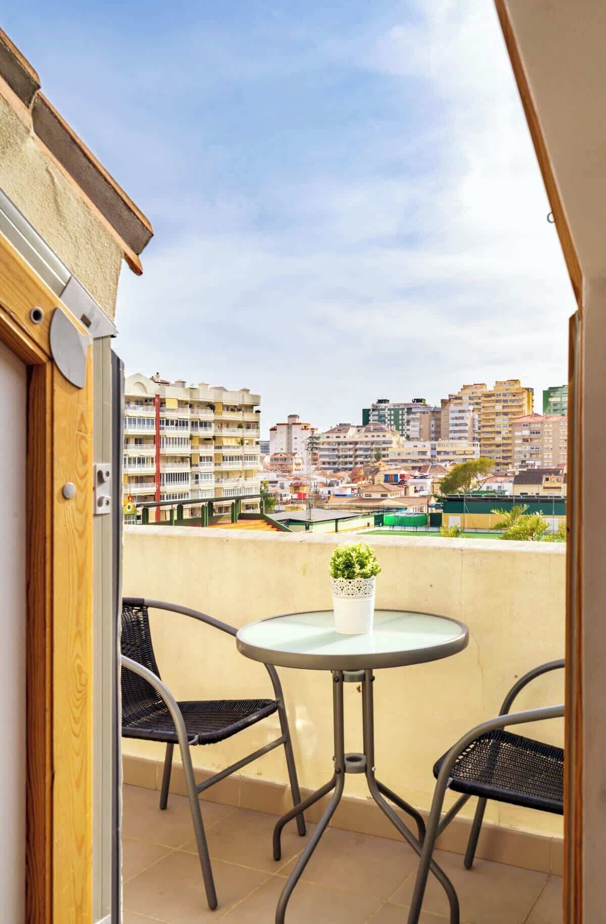 Un balcó amb una taula rodona i dues cadires, amb vista a un paisatge urbà ple d'edificis.