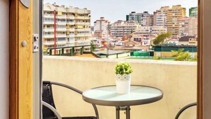 Un balcón con una mesa redonda y dos sillas, con vista a un paisaje urbano con varios edificios.