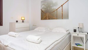 Una habitación de hotel con cama, mesita de noche, lámpara, un cuadro de un puente y un enchufe.