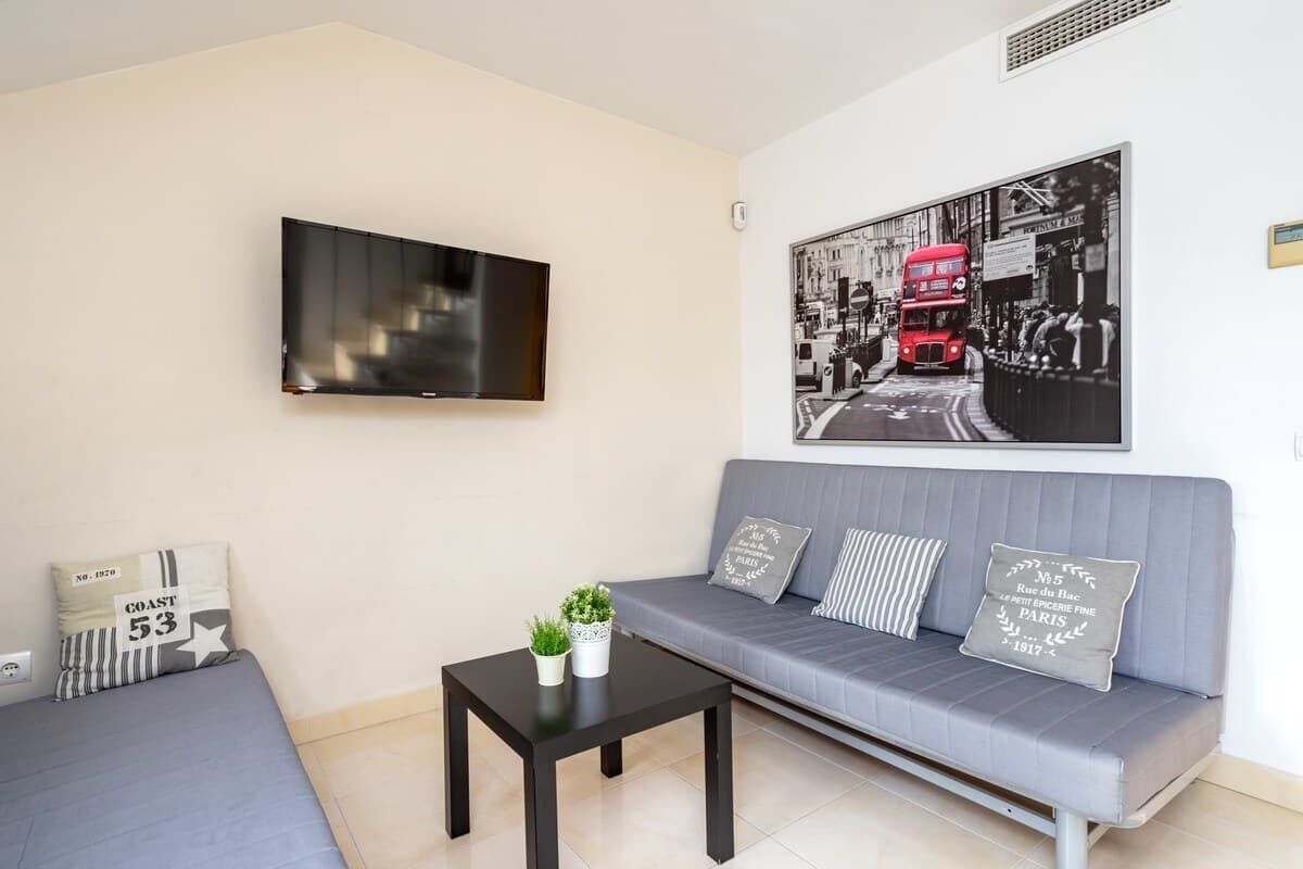 A modern living room with a grey sofa, a black coffee table, and a flat-screen TV mounted on the wall.