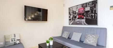 A modern living room with a grey sofa, a black coffee table, and a flat-screen TV mounted on the wall.