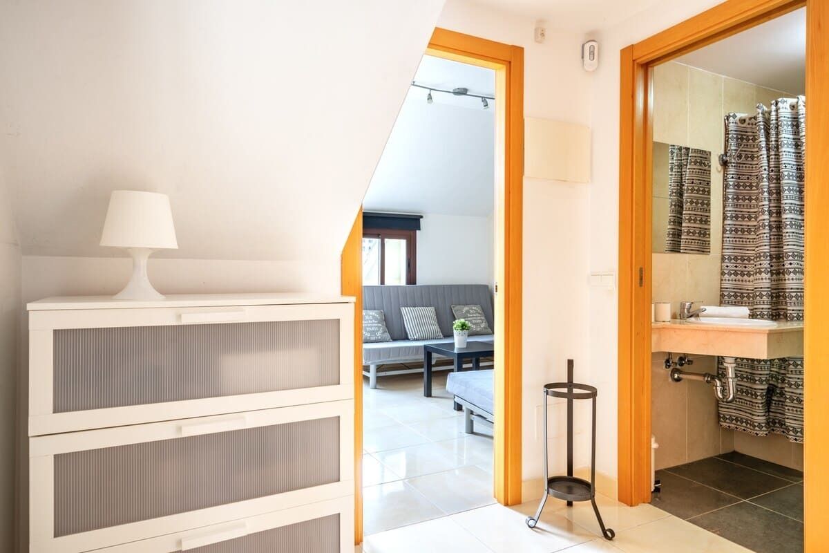 A modern room with a white cabinet, a lamp, a sofa, and a bathroom with patterned curtains.