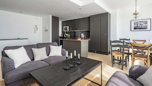 A modern living room with a grey sofa, a dark coffee table, and a dining area with wooden chairs and a small island with kitchen appliances. - Pool Penthouse in La Cala by Costarentals - Ref 19 (Las Lagunas de Mijas)