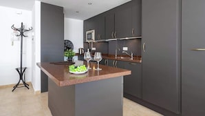 A modern kitchen with dark cabinetry, a granite countertop, and a small island with a bowl of fruit and two wine glasses. - Pool Penthouse in La Cala by Costarentals - Ref 19 (Las Lagunas de Mijas)