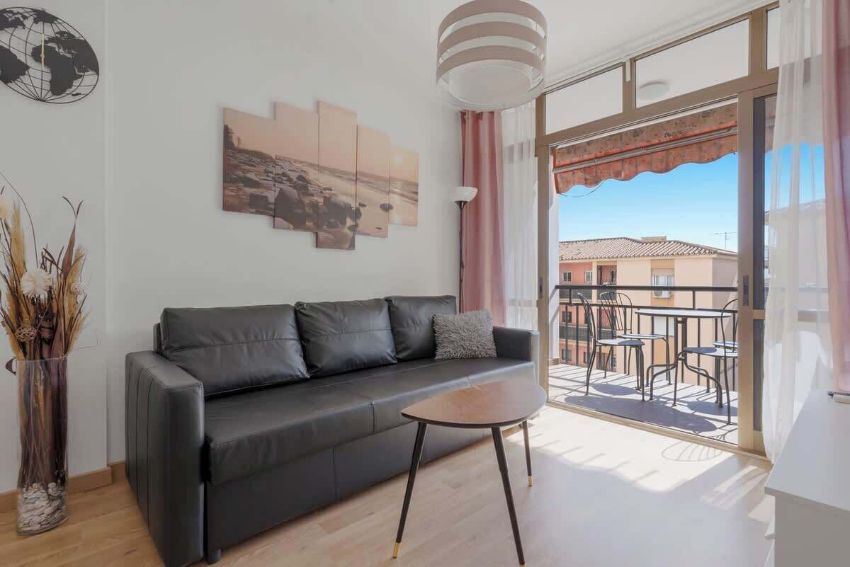 Ein modernes Wohnzimmer mit einer schwarzen Ledersofa, einem kleinen runden Tisch und einem großen Fenster mit Blick auf einen Balkon und Gebäude.