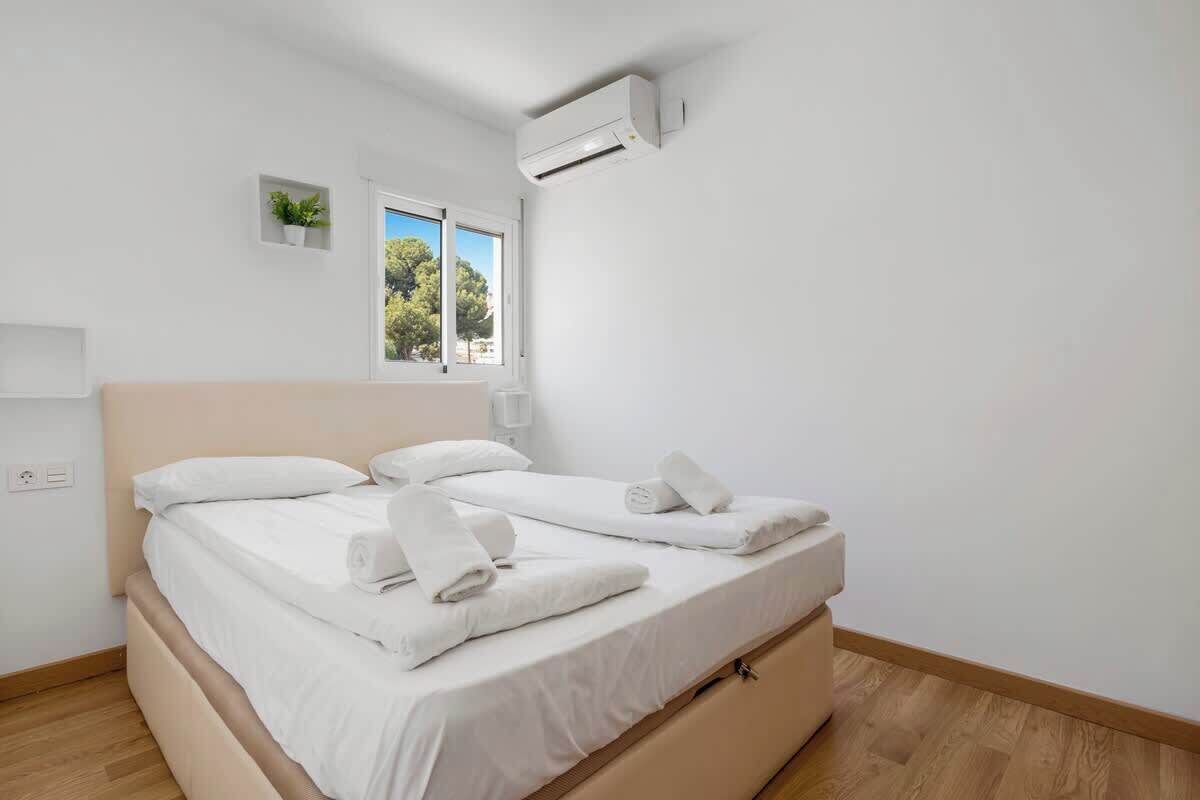 Habitación de hotel con dos camas, una ventana con vistas a árboles, un equipo de aire acondicionado y una planta pequeña en la pared.