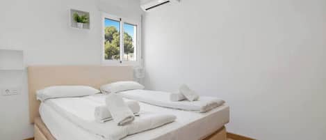 Habitación de hotel con dos camas, una ventana con vistas a árboles, un equipo de aire acondicionado y una planta pequeña en la pared.