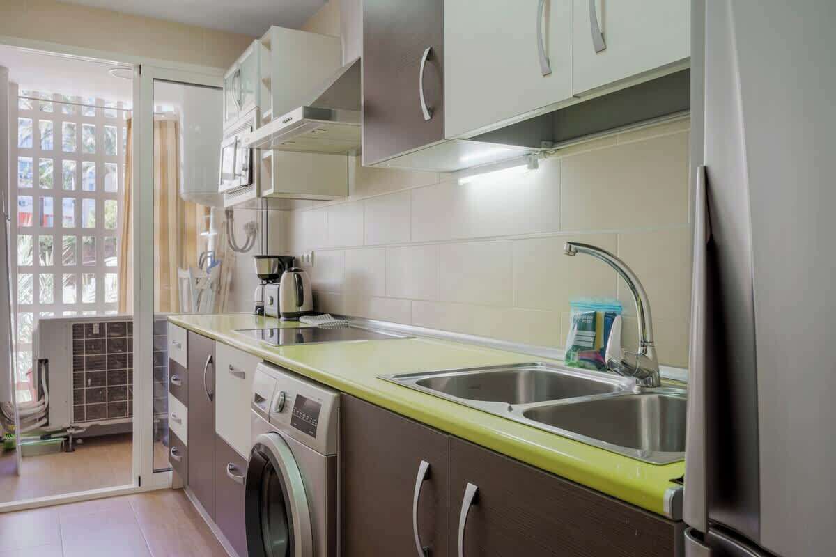 A compact kitchen with a washing machine, a sink, and a microwave.
