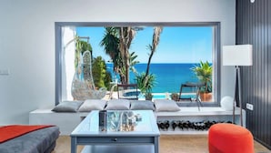 Un salon moderne doté d’une grande fenêtre donnant sur une piscine et la mer.