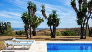 A pool area with lounge chairs and palm trees, overlooking a landscape with a distant view of a city. - Villa Sabah with sea views near Mijas Pueblo - REF 119 (Mijas)