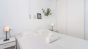 A minimalist hotel room with a bed, two bedside tables, a wall-mounted lamp, a potted plant, and a framed picture. - Beachclose Penthouse by Costarentals - Ref 15 (Fuengirola)