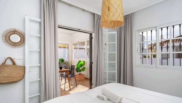Habitación de hotel con cama, lámpara de mimbre, espejo y vistas al exterior.