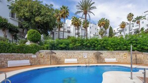 Piscina con muro de piedra y palmeras, rodeada de edificios blancos.