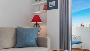 Un salon moderne avec un canapé, un bol en bois posé sur une table, une lampe rouge et une vue sur un balcon avec une chaise blanche.