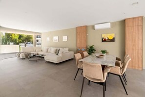 A modern living room with a sofa, coffee table, dining table, and chairs. There are framed pictures on the wall, a potted plant, and a wooden cabinet. - Castillo Sohail penthouse by Costarentals- Ref 147 (Fuengirola)