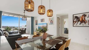 Un salon moderne avec une table à manger en verre, des suspensions en rotin et une vue sur la ville.