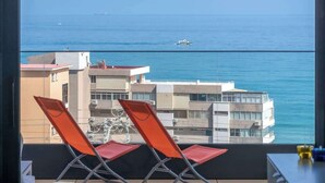 A balcony with two orange chairs and a hat, overlooking a body of water with buildings and a boat in the distance. - Modern Apartment w/ Pool & Gym Near Beach Access (Málaga)