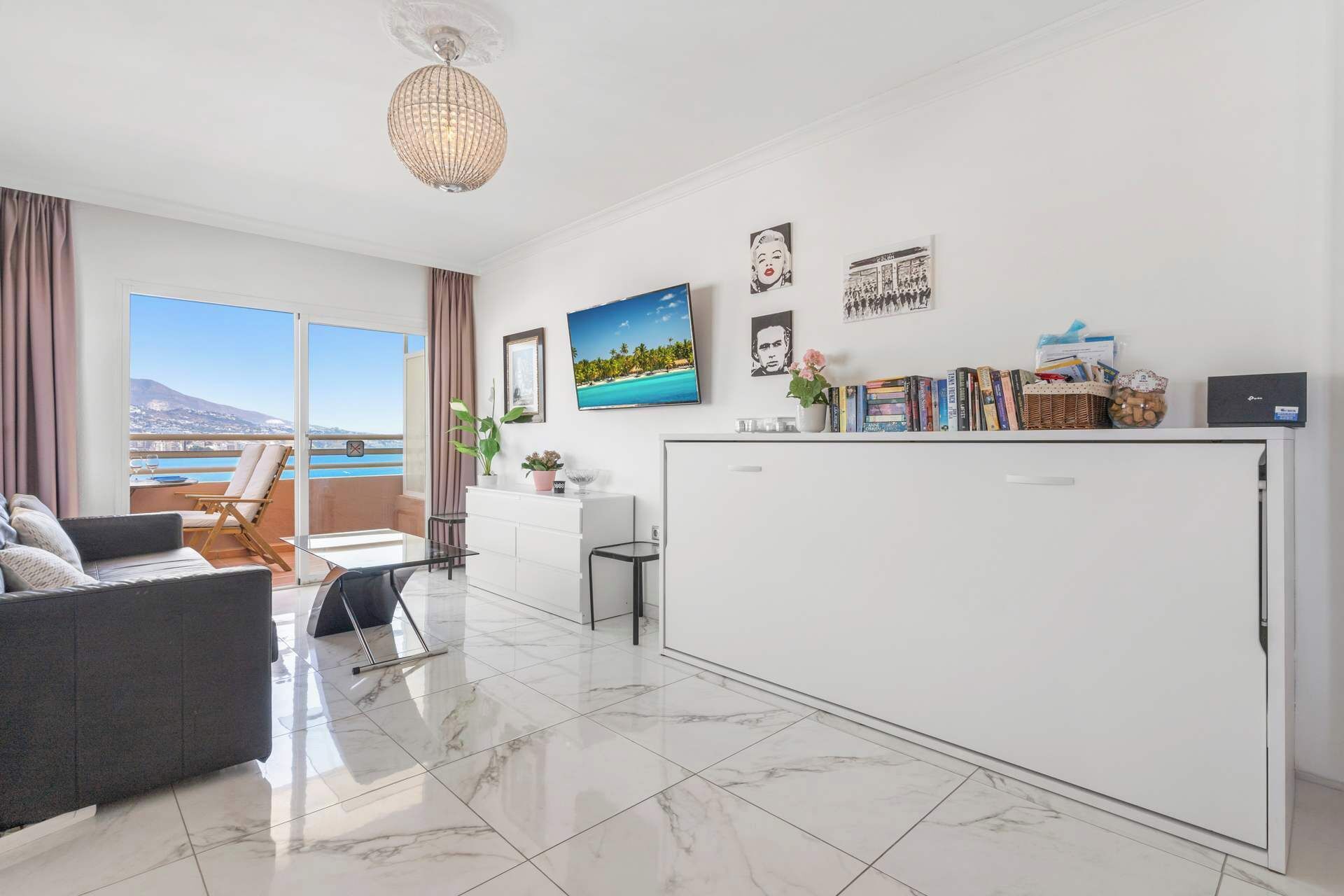 A modern living room with a sofa, a dining table, a kitchen area, and a view of the sea.
