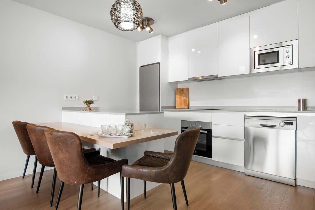 Una cocina moderna con armarios blancos, electrodomésticos de acero inoxidable y una mesa de comedor de madera con sillas.