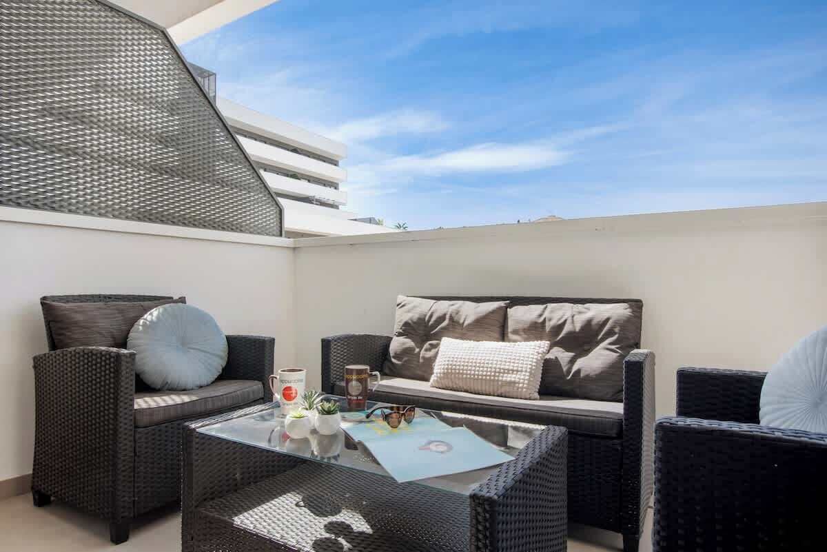 Una terraza en la azotea con mobiliario de mimbre, una mesa de centro de vidrio y una vista despejada del cielo.