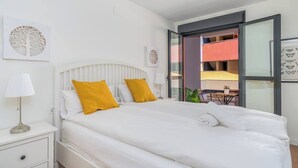 A modern hotel room with a large bed, white bedding, and two mustard-colored pillows. There is a white nightstand with a lamp, and artwork on the walls. - Central couples getaway by Costarentals - Ref 155 (Fuengirola)