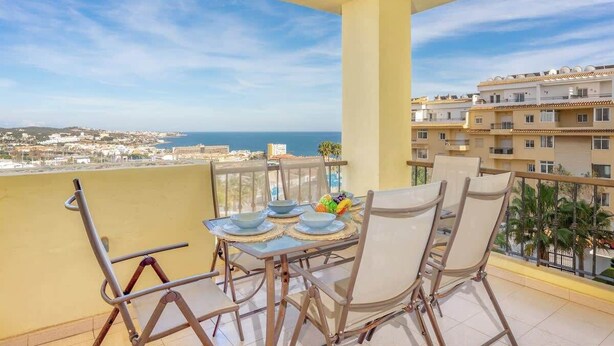 Un balcon avec une table dressée pour quatre personnes, offrant une vue sur le paysage urbain de la côte.