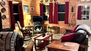 A cozy cabin interior with wooden walls, a fireplace, a television, and a dining area.