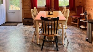 A wooden cabin interior with a dining table, chairs, a chandelier, and a sign reading "UPTACAMP".
