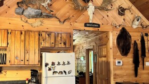 A rustic cabin interior with wooden walls, a ceiling-mounted light fixture, and a refrigerator displaying various animal figures.