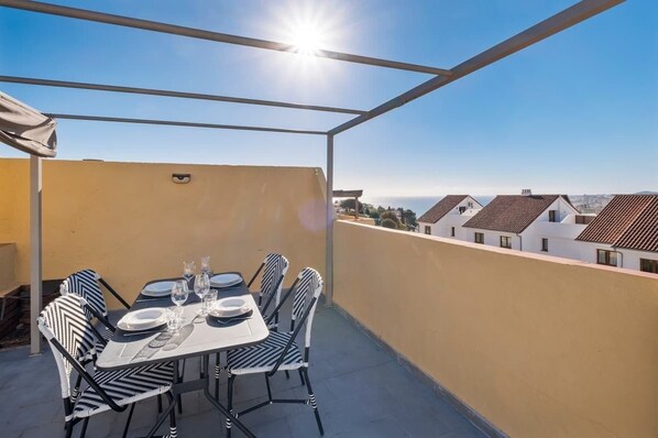 Eine Dachterrasse mit Esstisch, umgeben von einem Metallgeländer und freiem Blick auf die Stadtlandschaft.