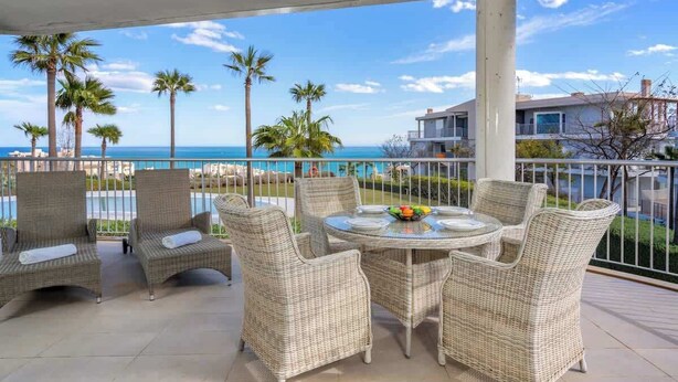 A covered outdoor seating area with wicker furniture and a table, overlooking a beach and ocean. - Sunny Terrace with Jacuzzi by Costarentals- Ref 26 (Benalmádena)