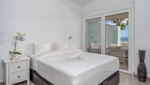 A modern hotel room with a large bed, a nightstand, a vase with flowers, and a view of the balcony and ocean. - Sunny Terrace with Jacuzzi by Costarentals- Ref 26 (Benalmádena)