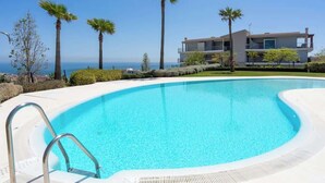 A modern pool with clear blue water, surrounded by palm trees and a view of the ocean. - Sunny Terrace with Jacuzzi by Costarentals- Ref 26 (Benalmádena)