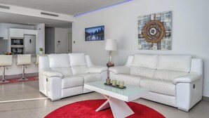 A modern living room with two white leather sofas, a coffee table, and a red rug. There is a painting on the wall and a lamp on the table. - Sunny Terrace with Jacuzzi by Costarentals- Ref 26 (Benalmádena)