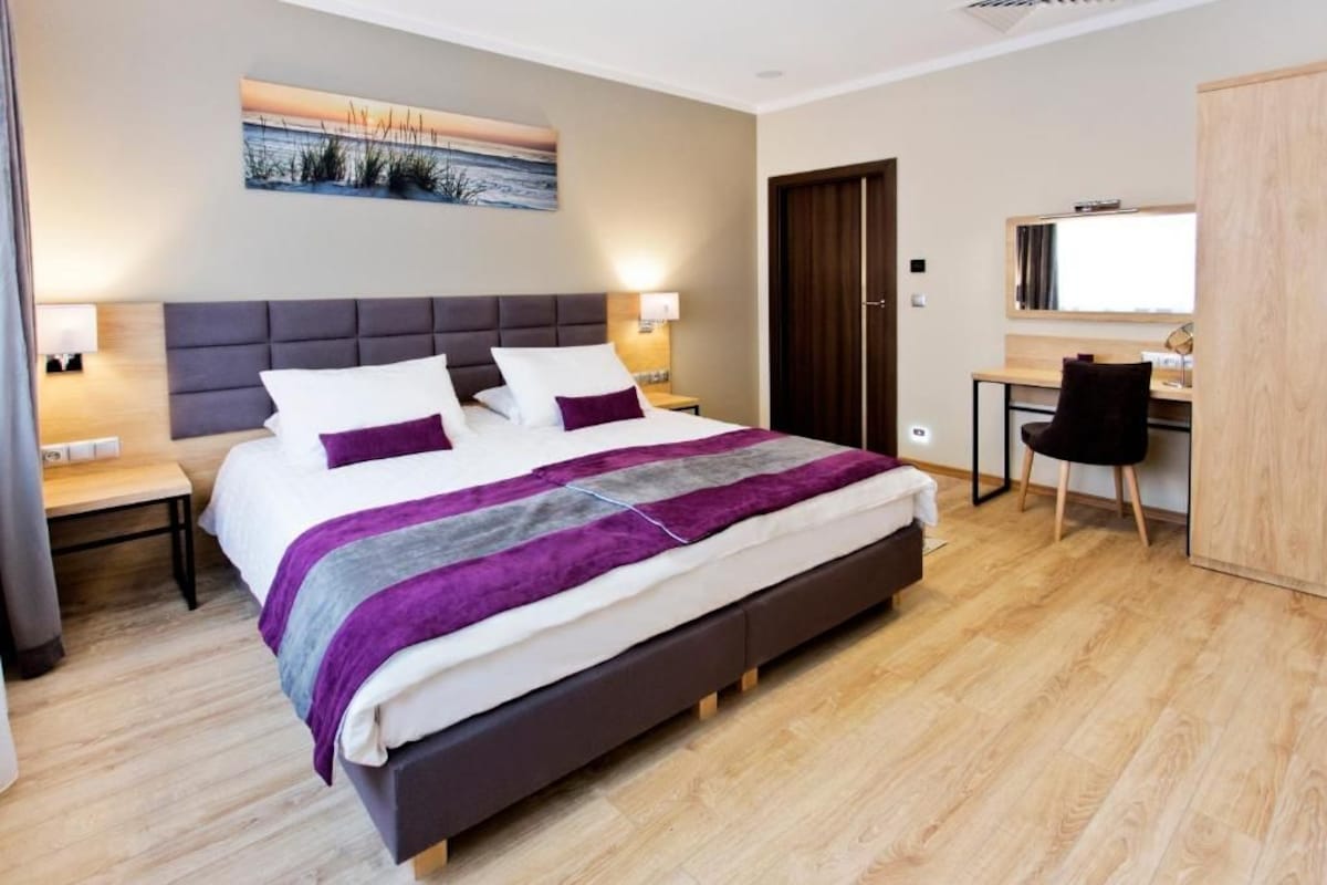 A modern hotel room with a large bed, a desk, and a chair.