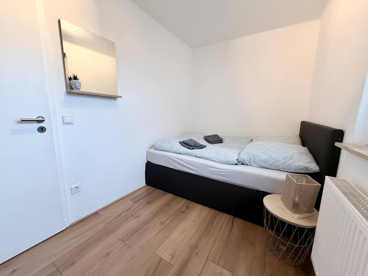 Een kleine, moderne slaapkamer met een bed, nachtkastje en een radiator.