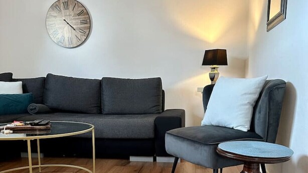 A modern living room with a dark grey sofa, a round coffee table, and a wooden floor. - FeWo Lindenallee – Modern & Ruhig (Nordhorn)