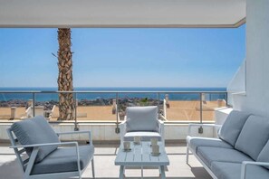 A balcony with white furniture, a table with cups, and a view of the sea and buildings.