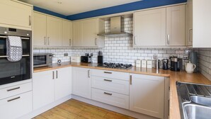 A modern kitchen with white cabinets, a wooden countertop, a built-in oven, a microwave, and a gas stove. - 12 The Gardens (Lyme Regis)