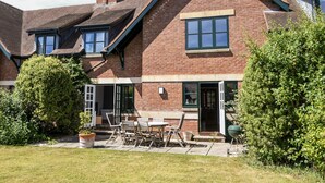 A two-story brick house with a large front porch, a chimney, and a garden with outdoor furniture. - 12 The Gardens (Lyme Regis)