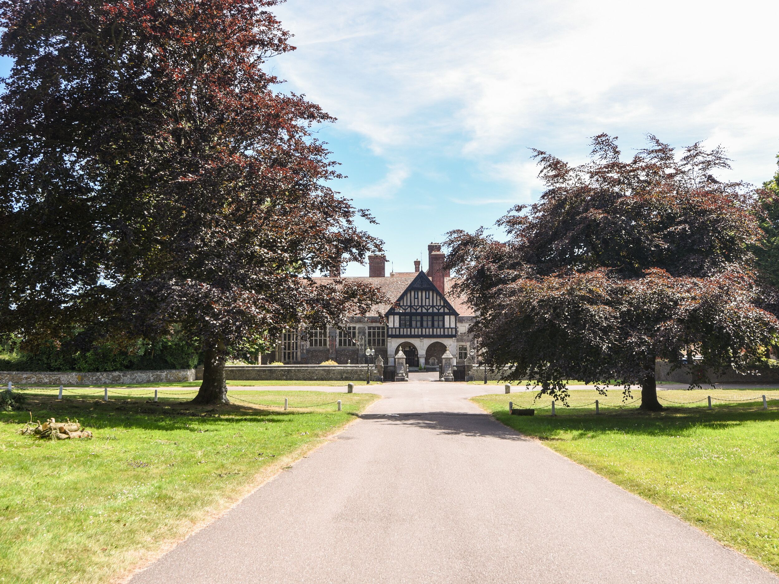 A pathway leading to a traditional Tudor-style building with a symmetrical facade, arched windows, and a central entrance.